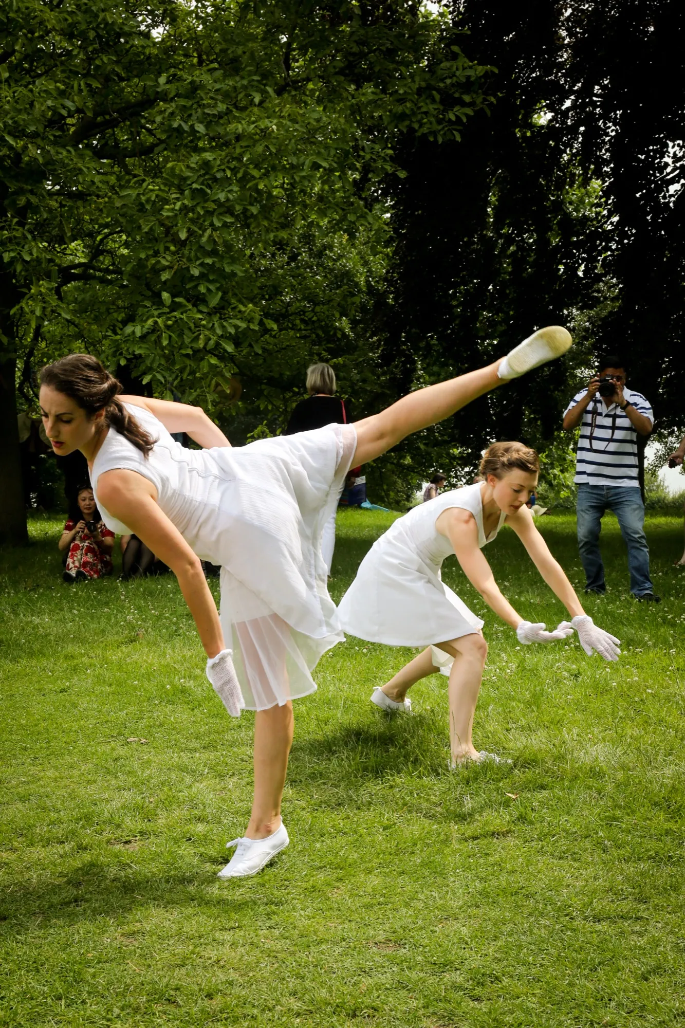Two dancers in white cartwheel across a sunlit lawn, A Curious Cakewalk