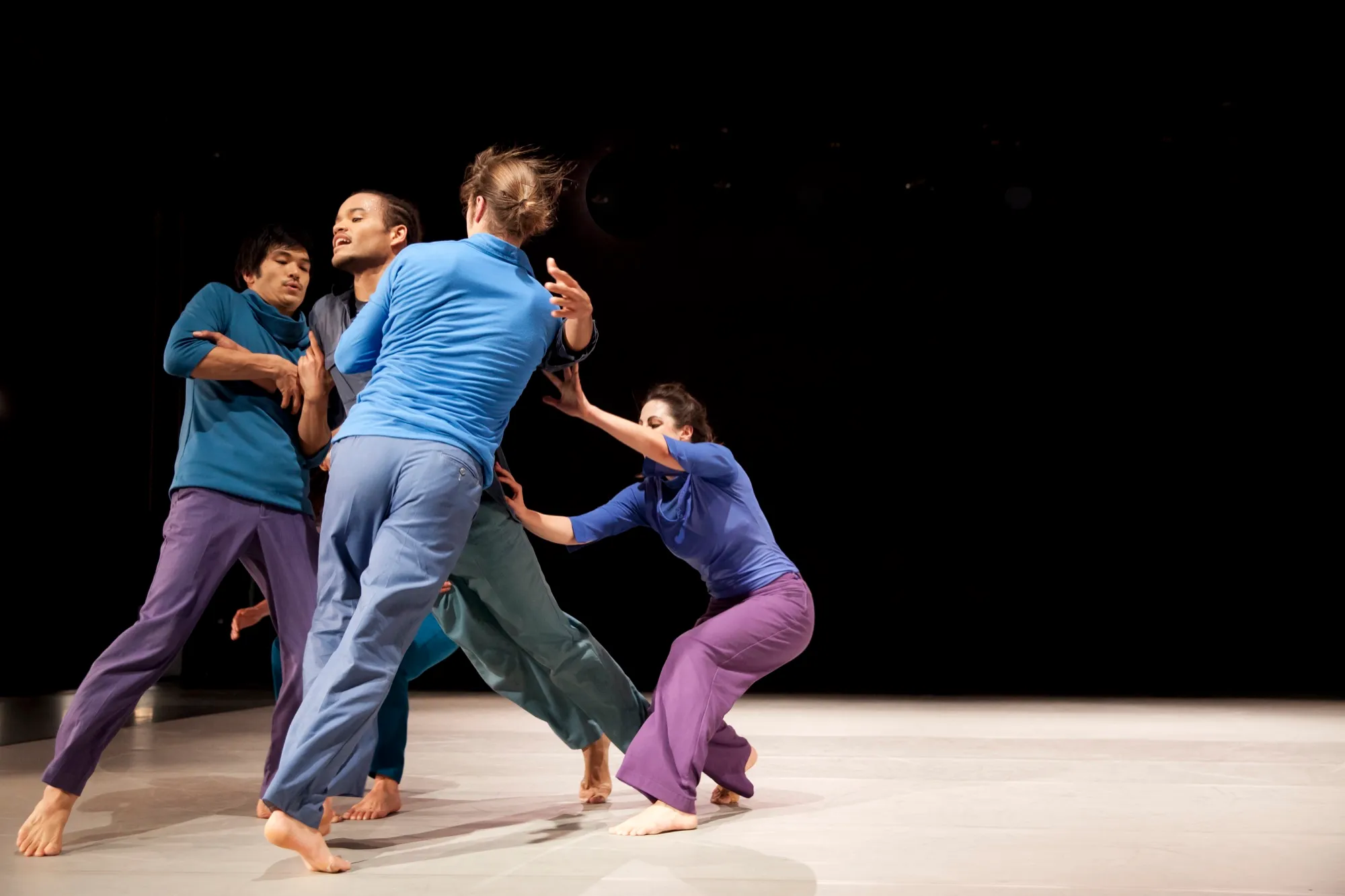 Five dancers in a tangle of colour on a dark stage, In the middle with you
